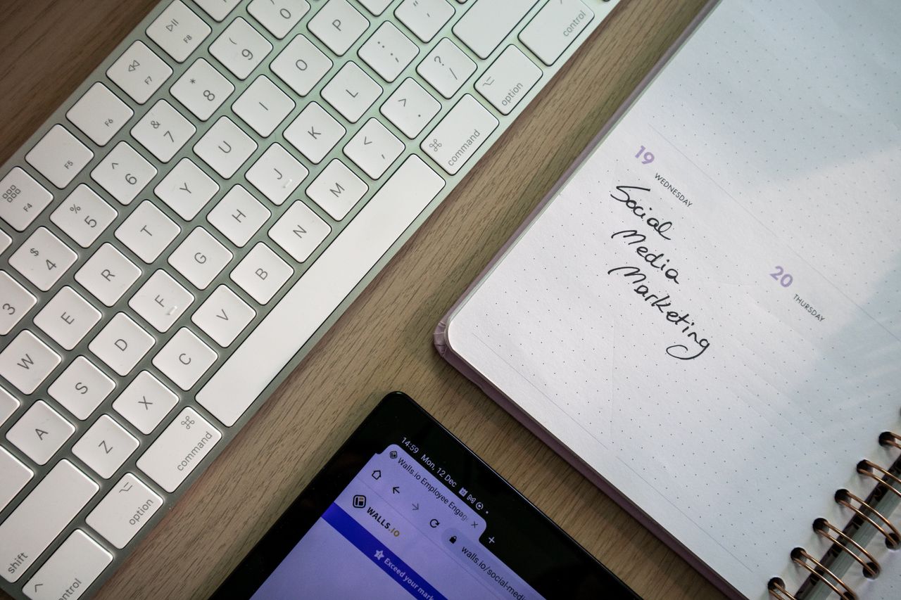 Vue de dessus d'un clavier, d'un agenda avec une note de marketing sur les réseaux sociaux, et d'une tablette posés sur un bureau.